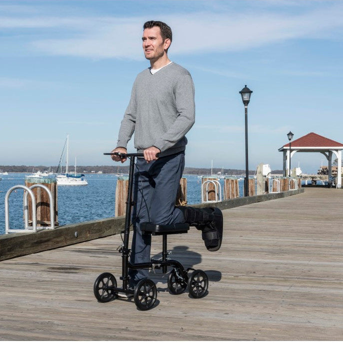 Man riding a scooter on a wooden pier with water and boats in the background