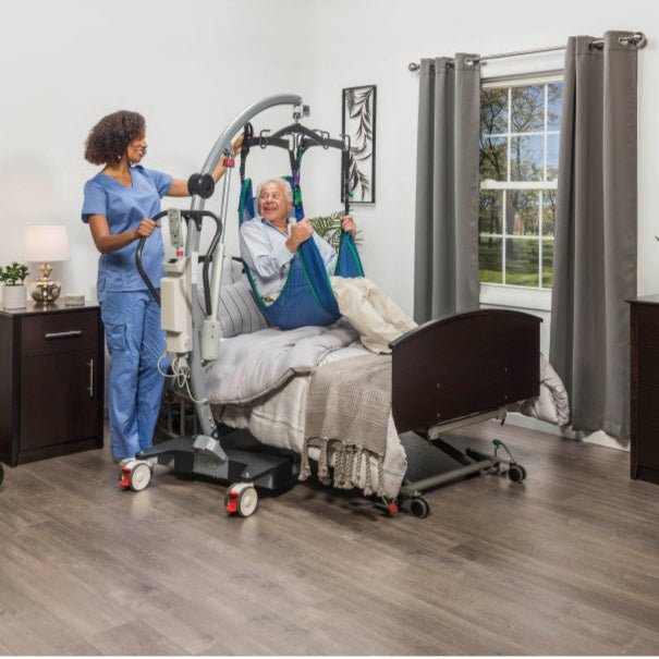 Caregiver assisting a patient in a hospital bed with medical equipment in a room.